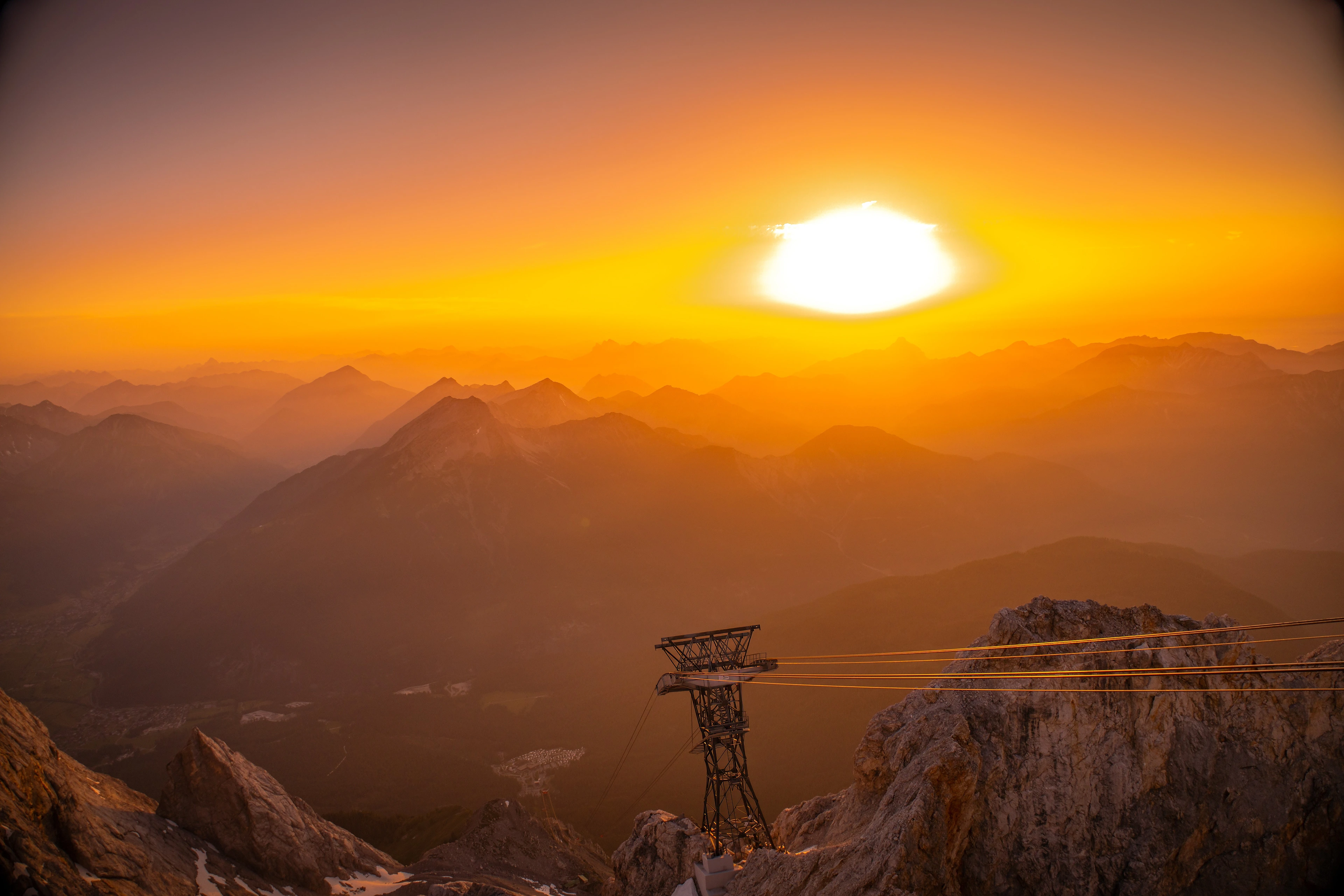 Blick von der Zugspitze auf eine Seilbahnstütze während eines goldenen Sonnenuntergangs.