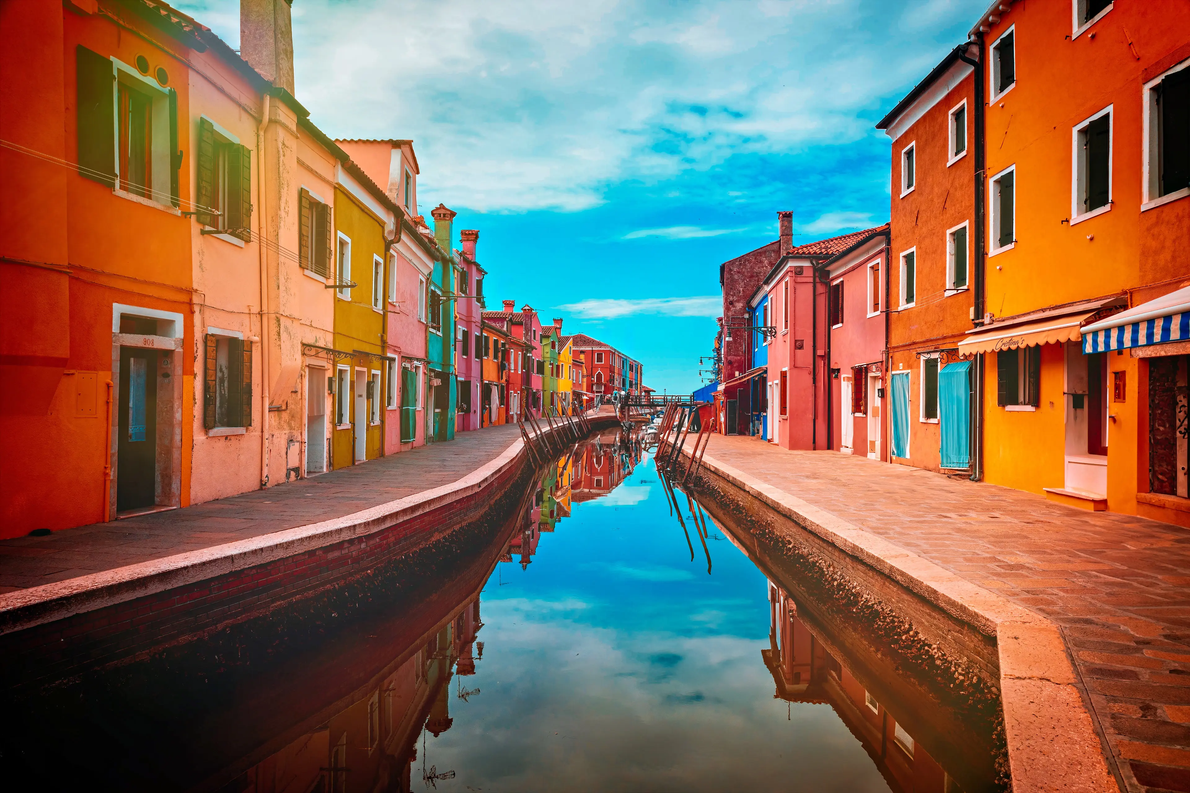 Farbenfrohe Häuserfronten entlang eines Kanals auf der Insel Burano, Venedig, mit Spiegelung im Wasser.