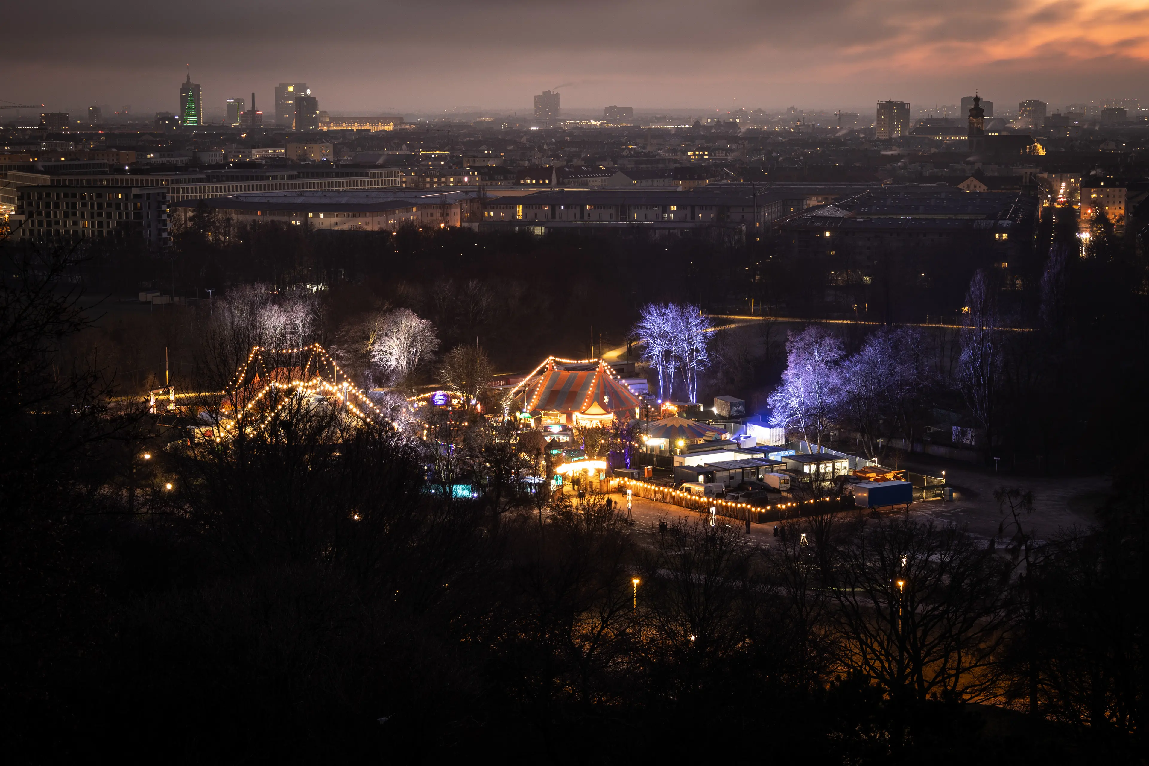 Nächtliche Luftaufnahme eines beleuchteten Weihnachtsmarkts (Märchenbazar) in München.
